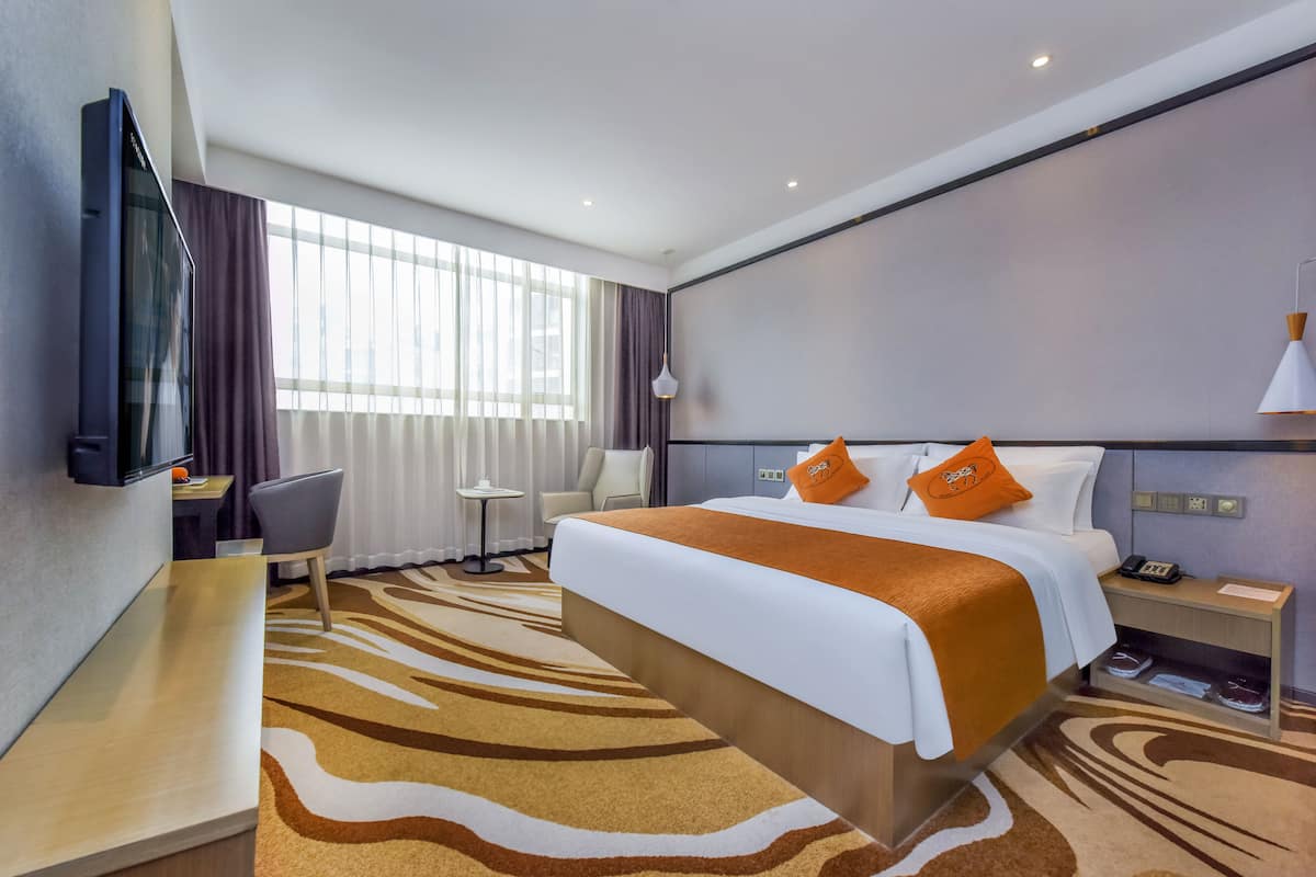 A hotel room with a large bed, a desk, a chair, a TV, and a window with curtains.