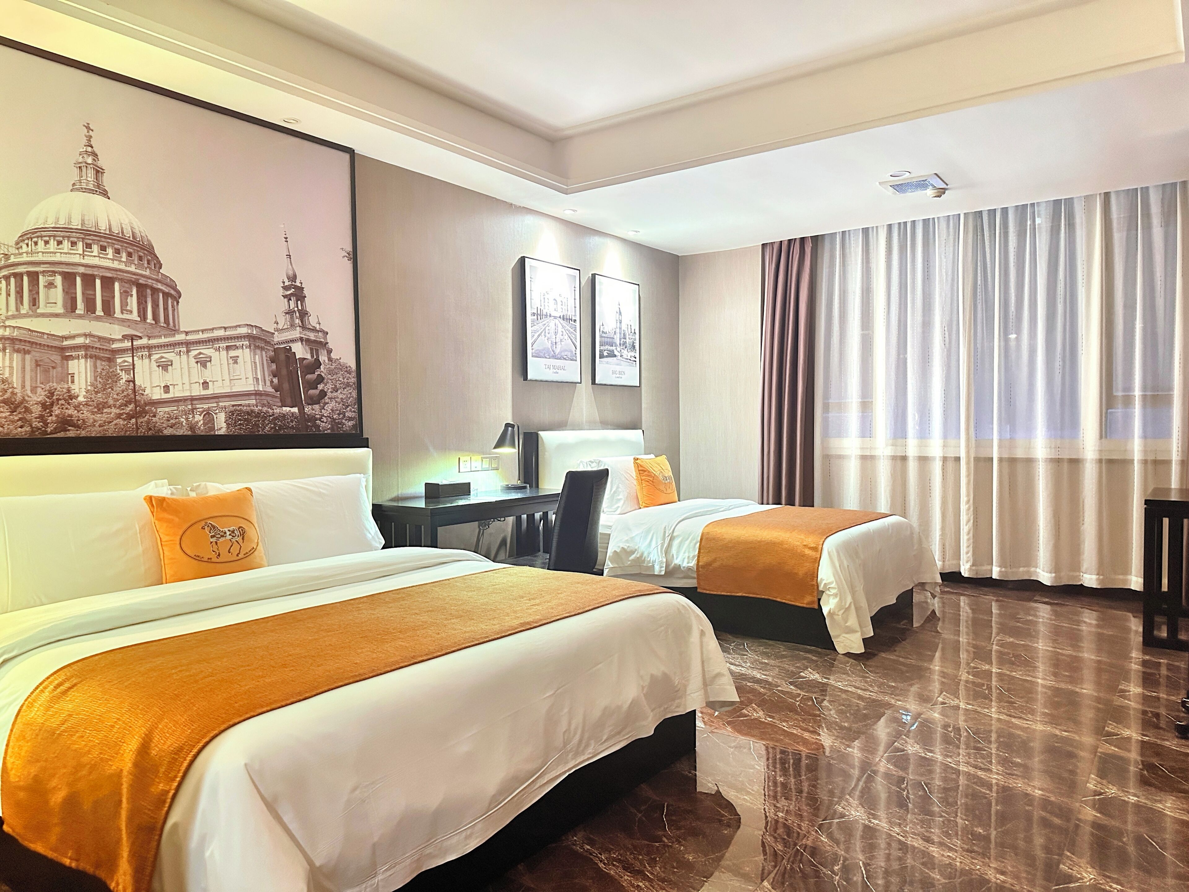 Ein Hotelzimmer mit zwei Betten, einem Schreibtisch, einem Stuhl und einem großen Fenster mit Vorhängen.
