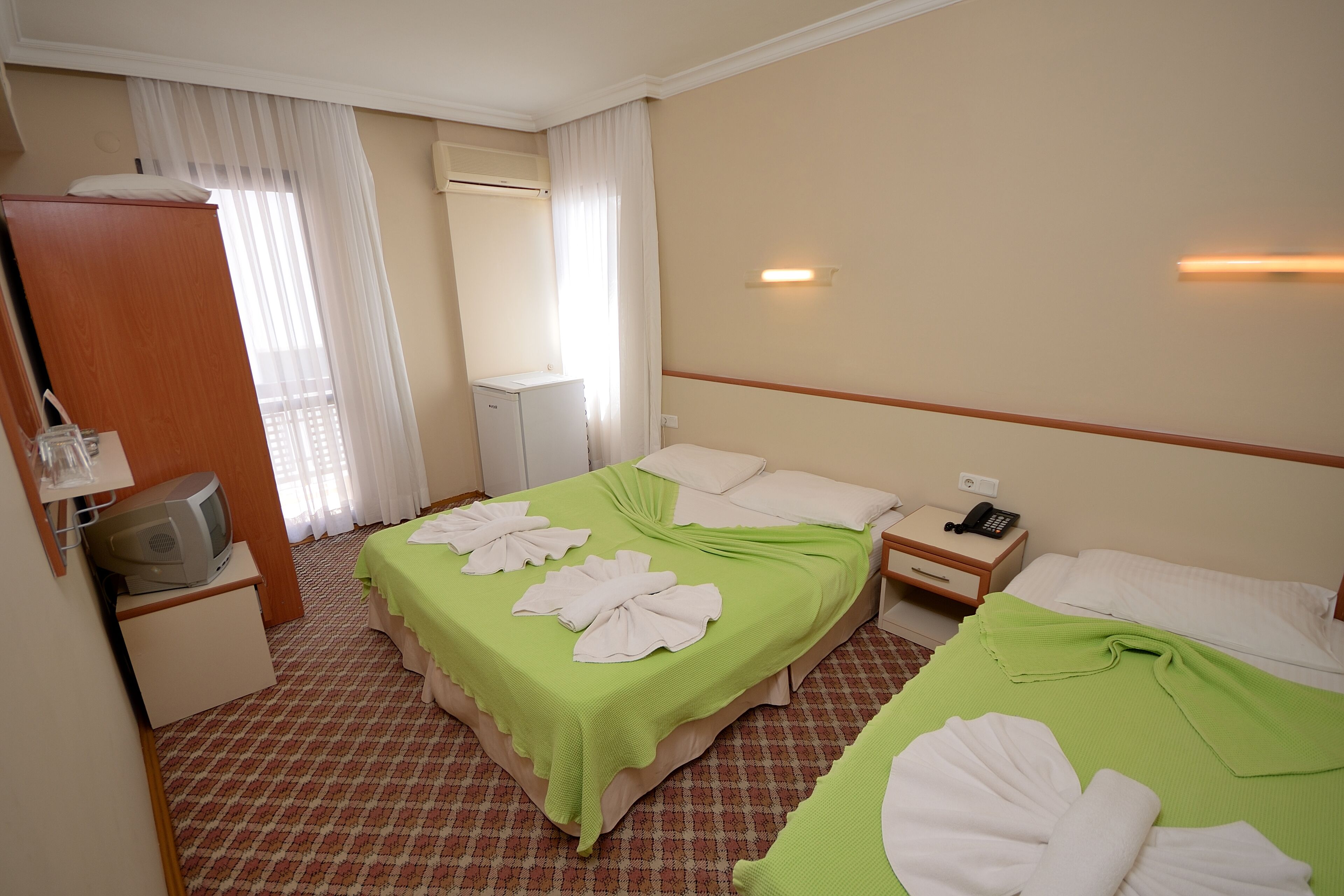Habitación de hotel con dos camas, un televisor, una mesita de noche y una ventana con cortinas.