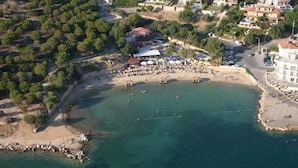 An aerial view of a coastal area with a beach, boats, and buildings. - Kerman Hotel (Cesme)