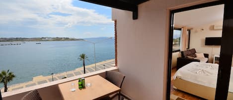 A balcony with wicker furniture, a table, and a view of the sea.