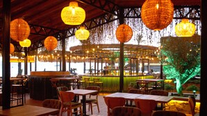 An indoor restaurant with wooden tables and chairs, hanging lanterns, and a green-lit tree. - Kerman Hotel (Cesme)