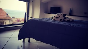A bedroom with a large window, a bed, a flat-screen TV, and a bottle on a shelf. - Casa Aurora (Taormina)