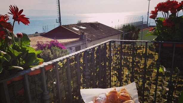 A balcony with a table set with bread, eggs, and fruit. - Casa Aurora (Taormina)
