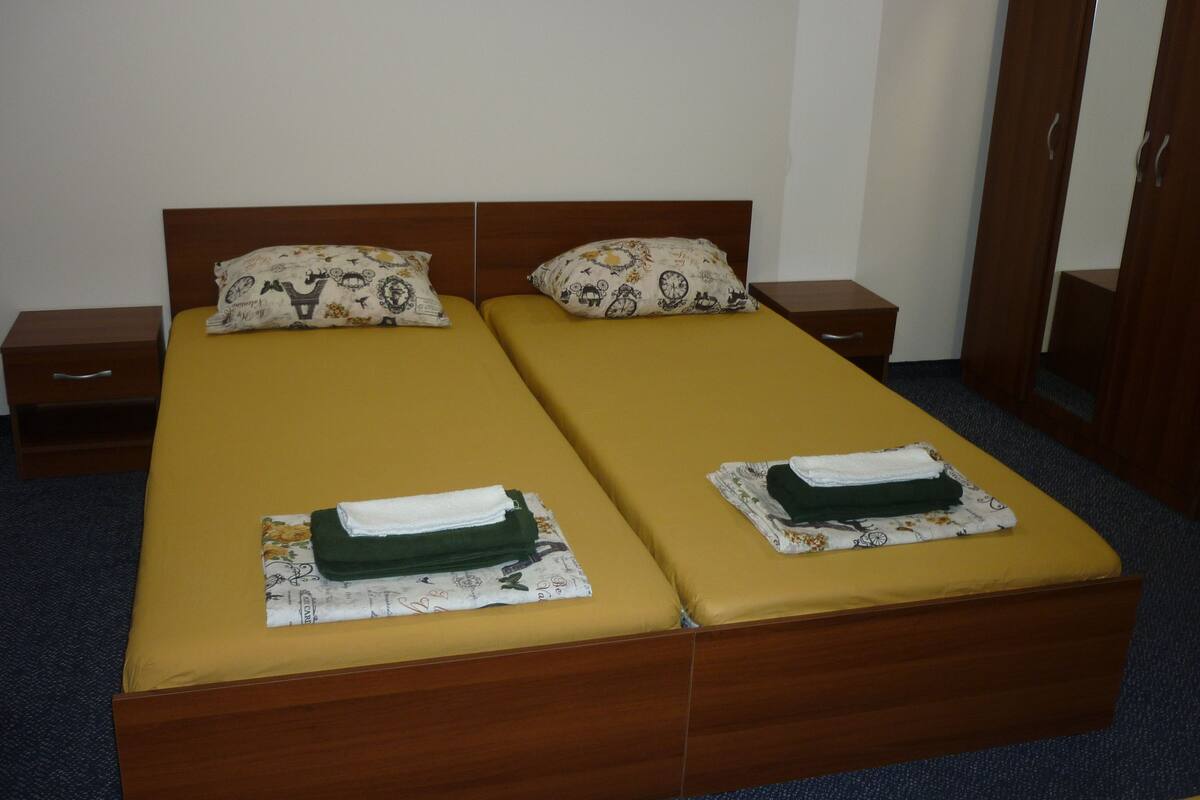 A double bed with yellow bedding and patterned pillows, a wooden nightstand, and a wooden wardrobe.