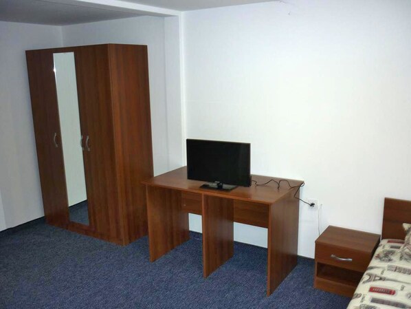 A room with a wooden desk, a television, a wardrobe, and a bed. - YALTA guesthouse (Ruse)