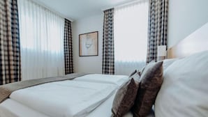 A hotel room with a bed, plaid curtains, a framed picture on the wall, and a bedside table with a lamp. - Hotel Ars Vivendi München (Munich)