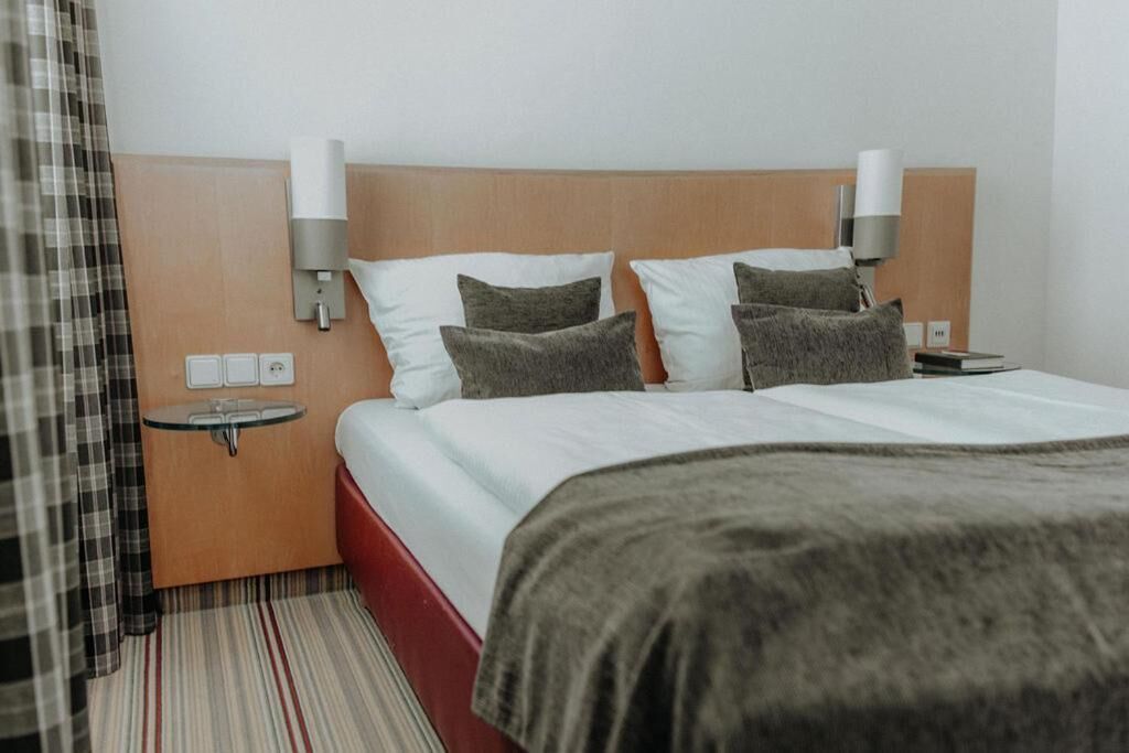 Habitación de hotel con cama, dos mesitas de noche, una lámpara de pared y un enchufe.