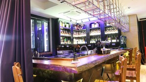 A bar area with a high counter, wooden chairs, and shelves stocked with bottles. - Grand Belllo Hotel JBCC (Johor Bahru)