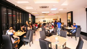 A spacious restaurant with multiple tables and chairs, a modern ceiling design, and large windows on one side. - Grand Belllo Hotel JBCC (Johor Bahru)