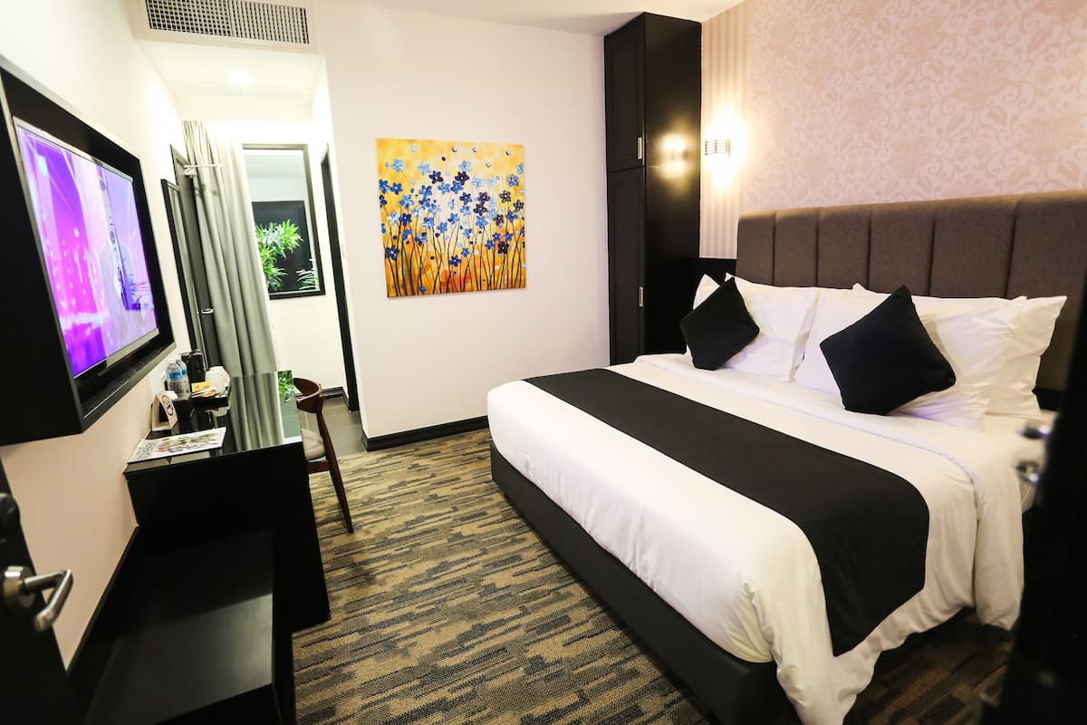Une chambre d’hôtel avec un grand lit, un bureau avec un ordinateur, une télévision et un tableau au mur.