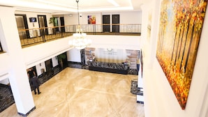 A hotel lobby with a marble floor, a reception desk, a chandelier, and a large painting on the wall. - Grand Belllo Hotel JBCC (Johor Bahru)