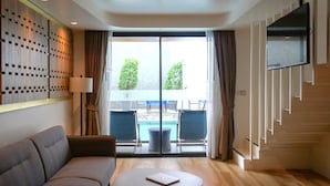 A modern hotel room with a sofa, a round table, a TV mounted on the wall, and a view of an outdoor swimming pool. - Wintree City Resort Chiang Mai (Chiang Mai)