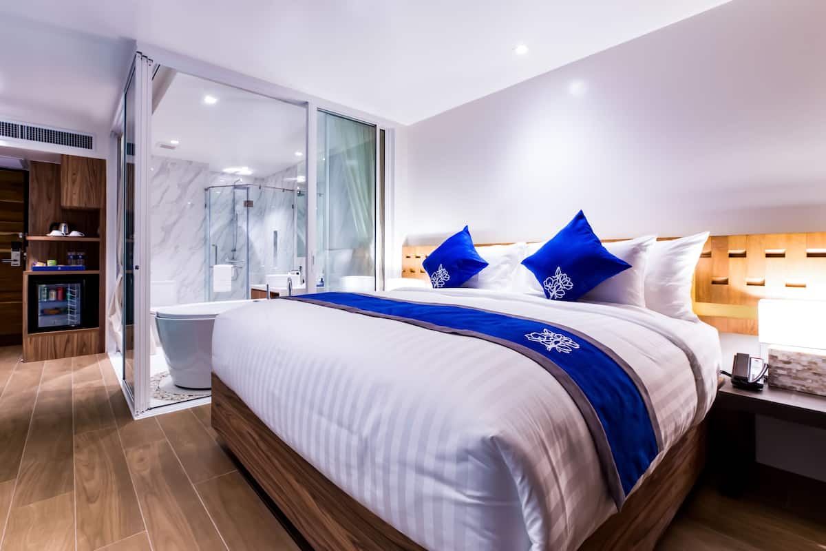 A modern hotel room with a large bed, a glass shower enclosure, and a wooden wardrobe.
