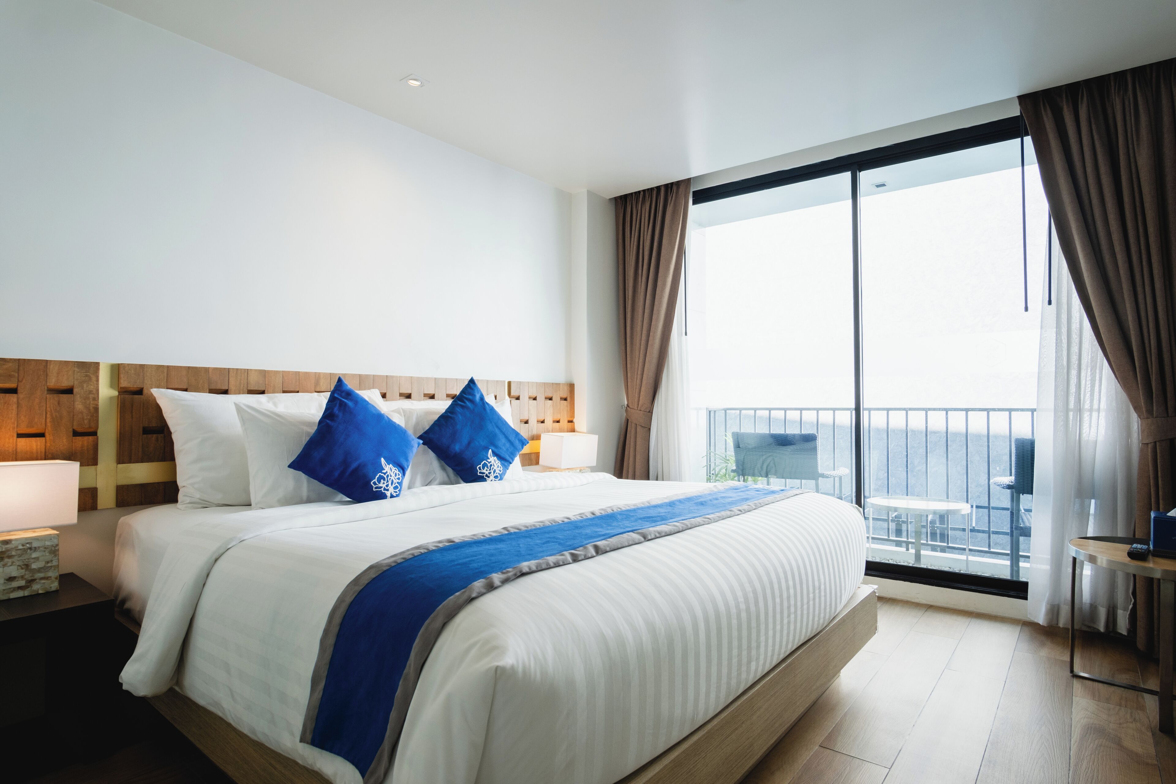 A hotel room with a large bed, a wooden headboard, a balcony with a view, and a small table with a lamp.