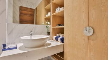 Un baño con un lavamanos grande y blanco, estantes de madera con toallas, y una pared con azulejos de mármol.