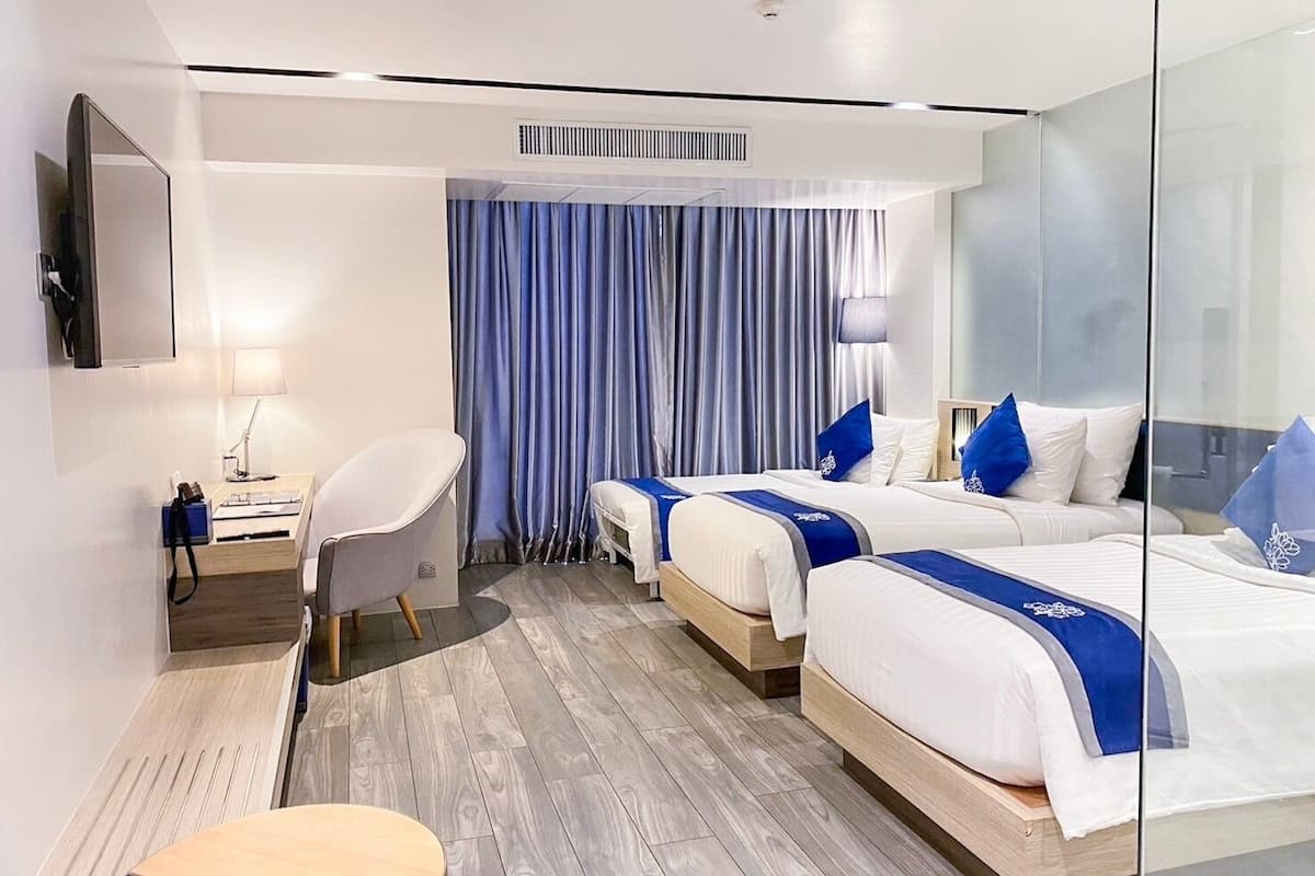 A hotel room with two beds, a desk, a chair, and a television.