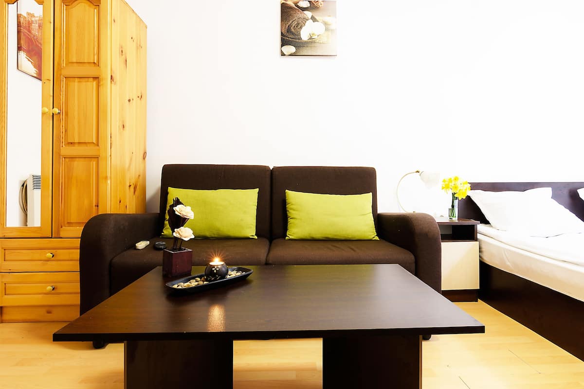 A room with a brown sofa, green cushions, a wooden table with a candle, and a bed with white bedding.