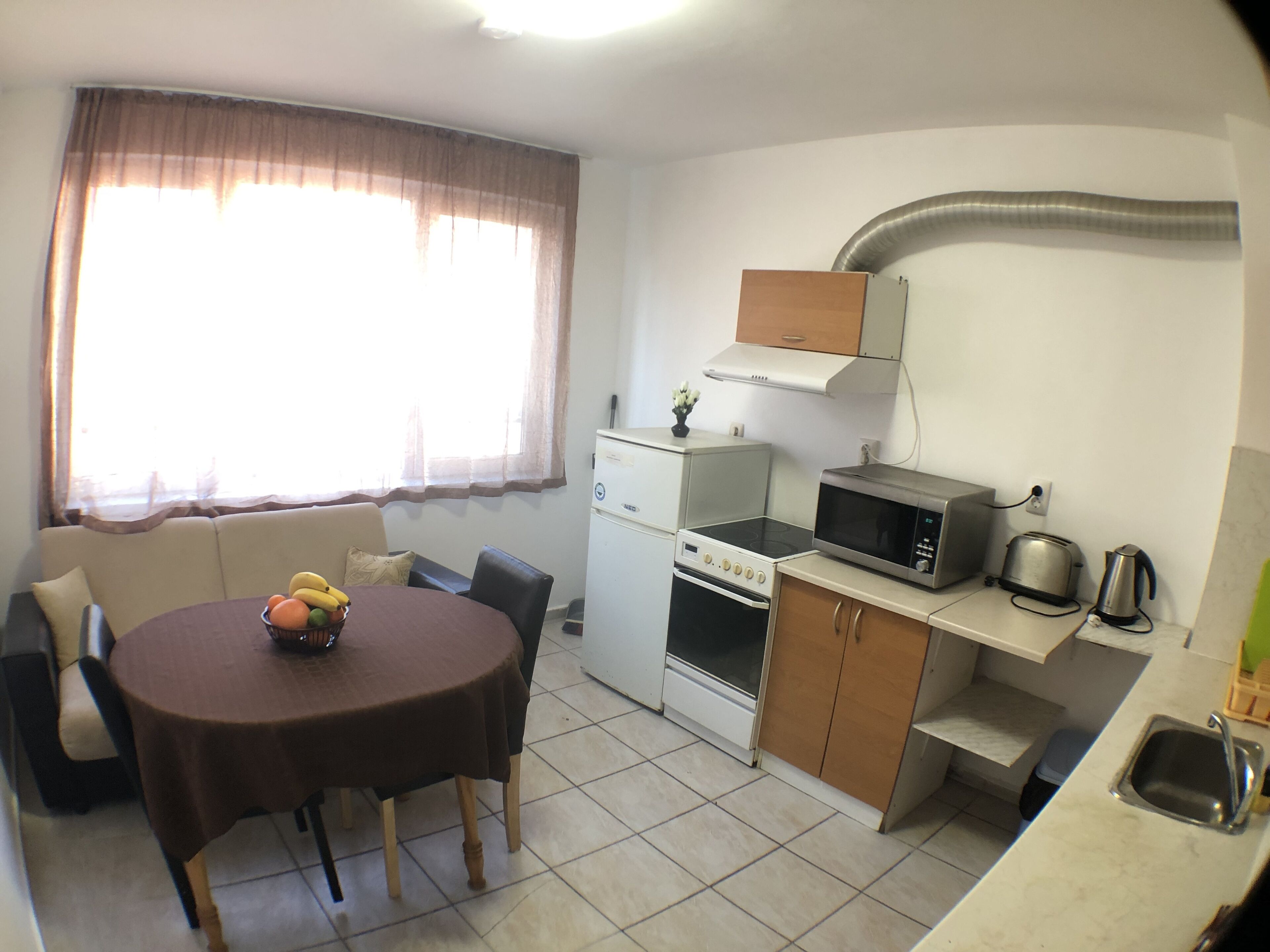 A compact kitchen with a stove, microwave, and toaster. There's a dining table with chairs and a small fruit bowl.