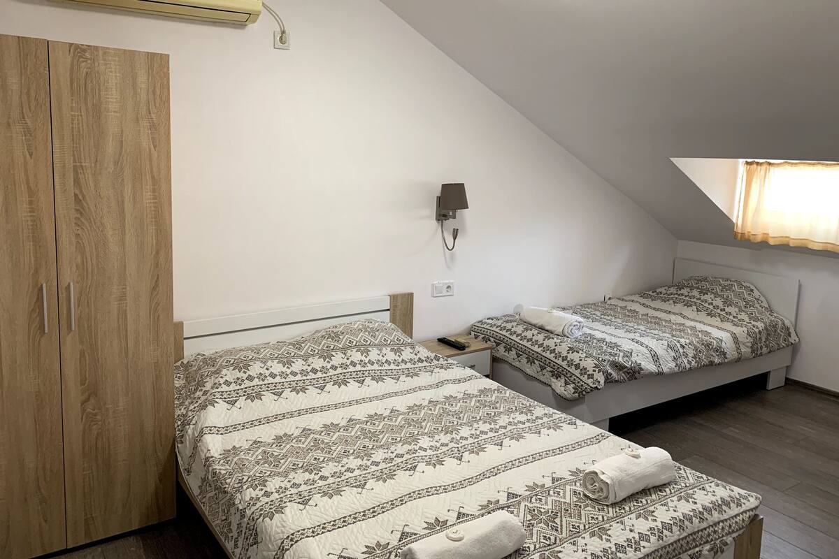 A bedroom with two beds, a wardrobe, an air conditioner, a wall-mounted lamp, and a window with curtains.