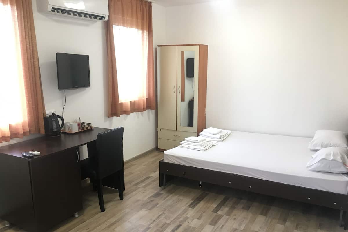 A bedroom with a bed, a desk, a chair, a wardrobe, and a television.