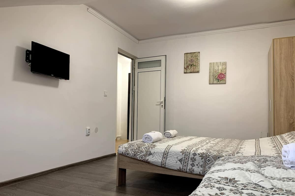 A bedroom with a bed, a TV mounted on the wall, a door, and a small artwork on the wall.