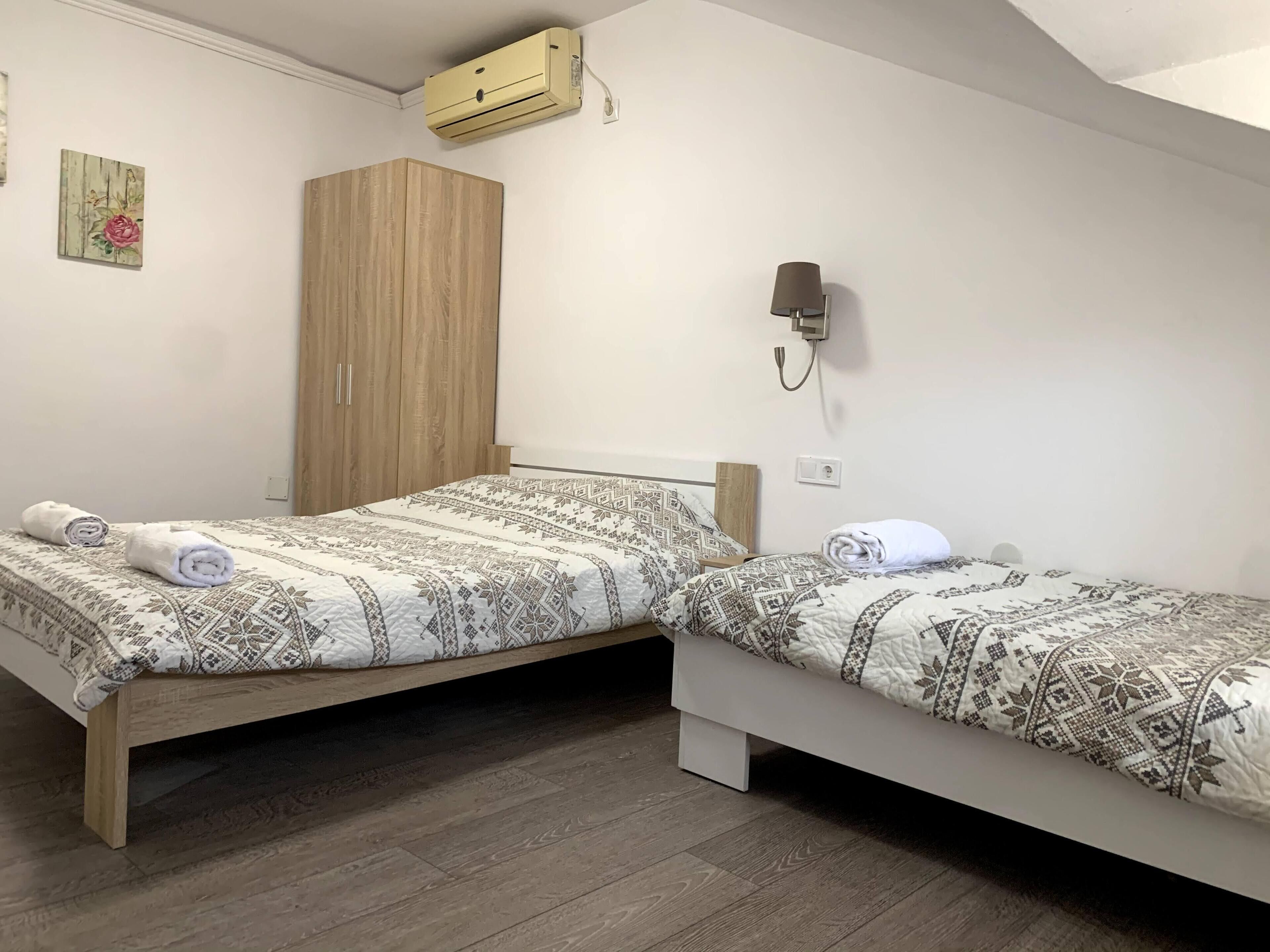 A room with two beds, a wooden wardrobe, an air conditioning unit, and a wall-mounted lamp.
