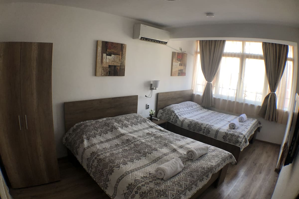 A hotel room with two beds, a wardrobe, an air conditioning unit, and artwork on the walls.