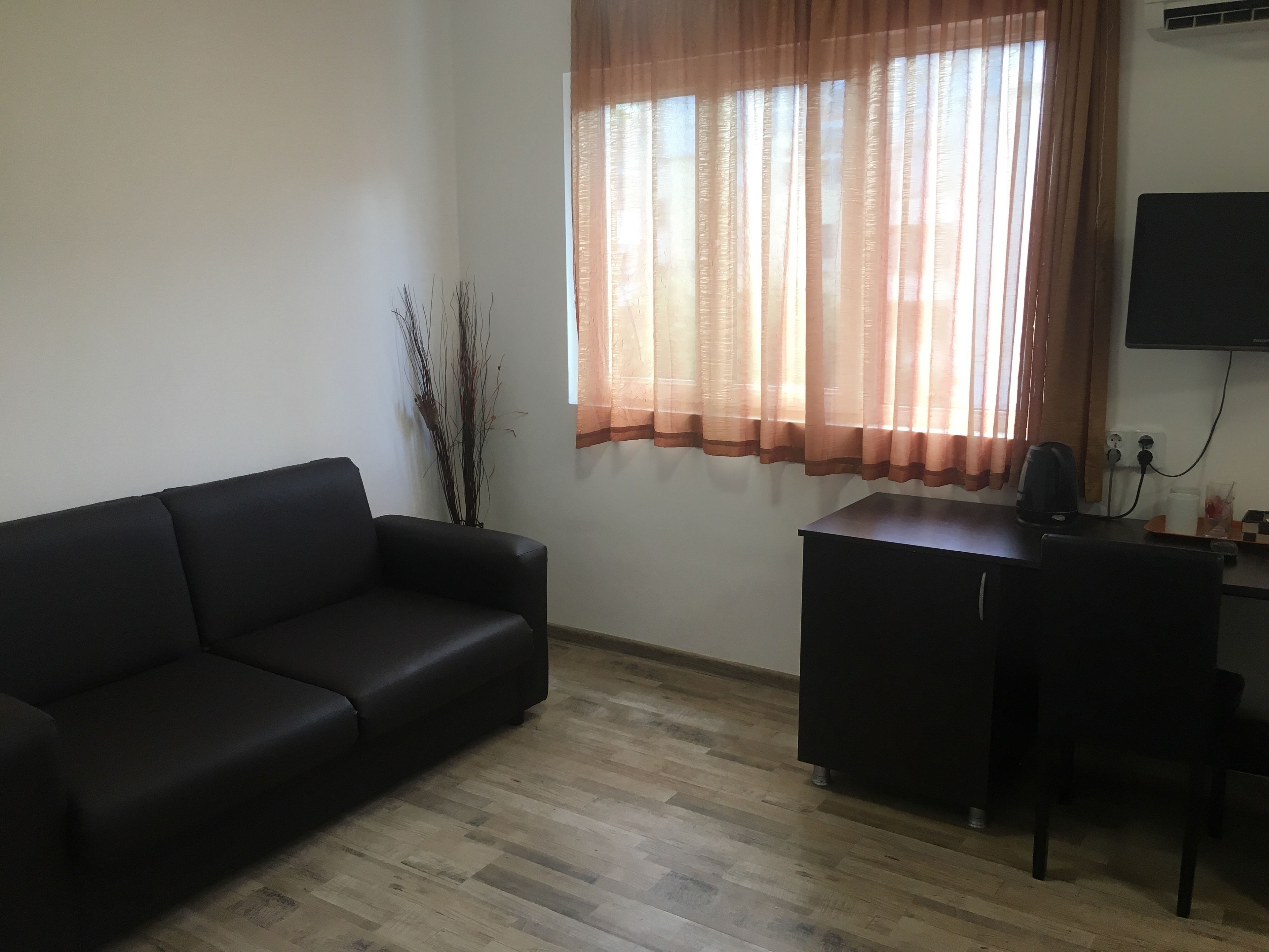 Ein Zimmer mit einer schwarzen Ledersofa, einem Holztisch und einem an der Wand befestigten Fernseher.