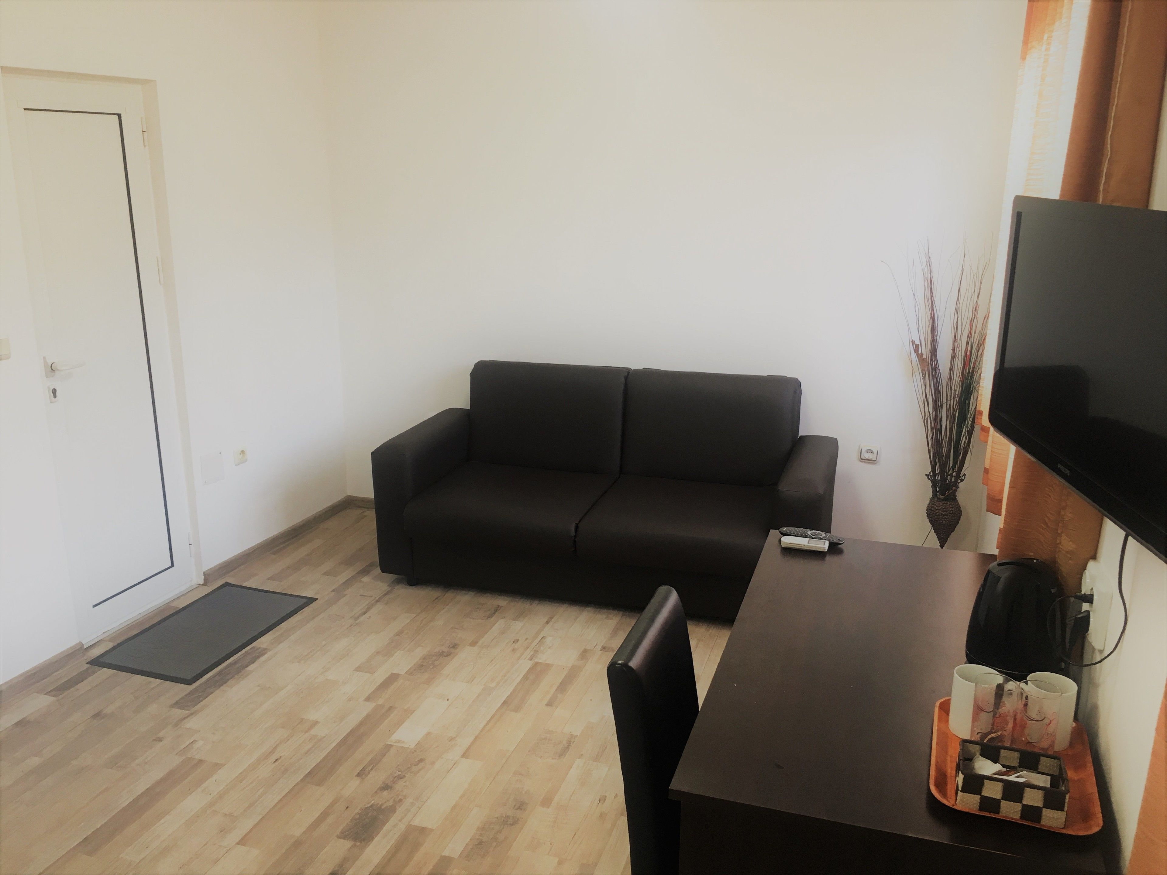 Una sala de estar con un sofá negro, una mesa de centro de madera y un televisor montado en la pared.