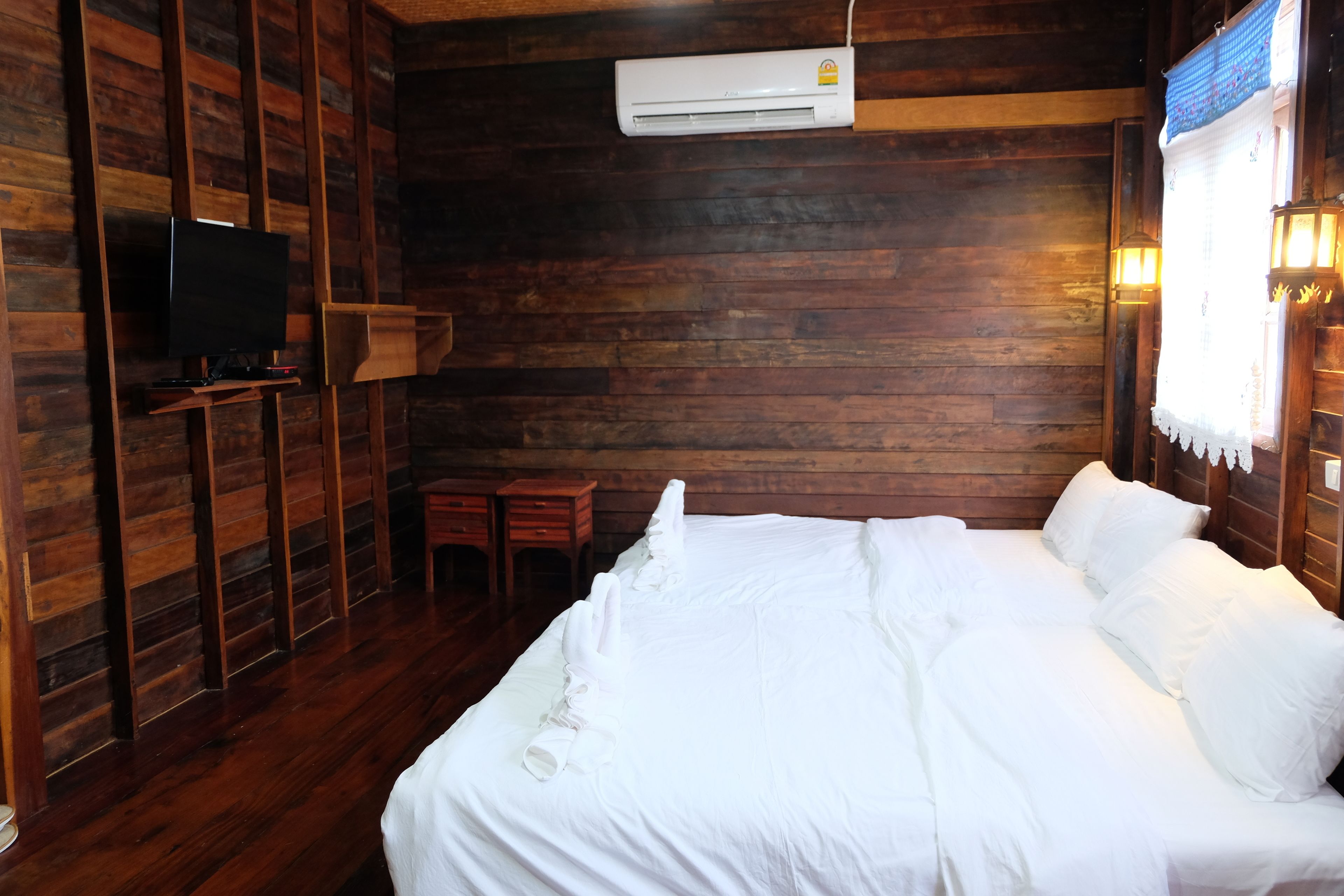 Una habitación con paneles de madera, una cama, un televisor, una mesita y un aire acondicionado.
