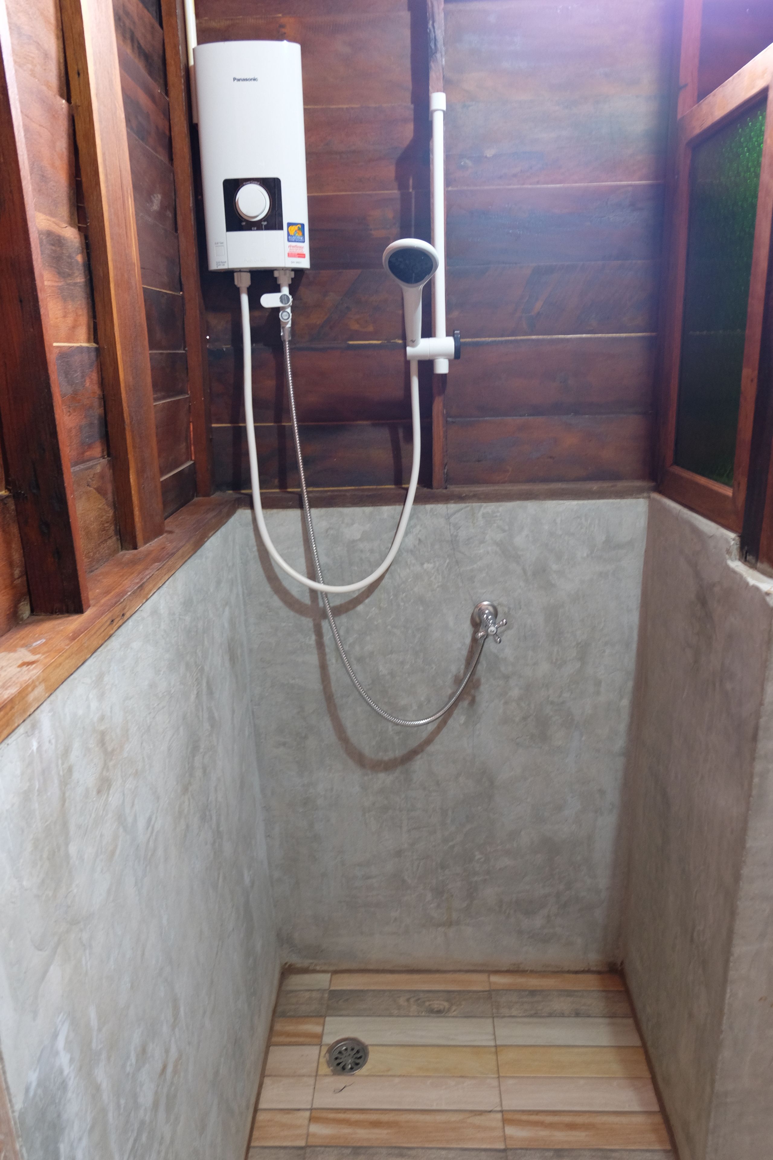 A small, enclosed shower area with a built-in water heater, a handheld showerhead, and a drain.