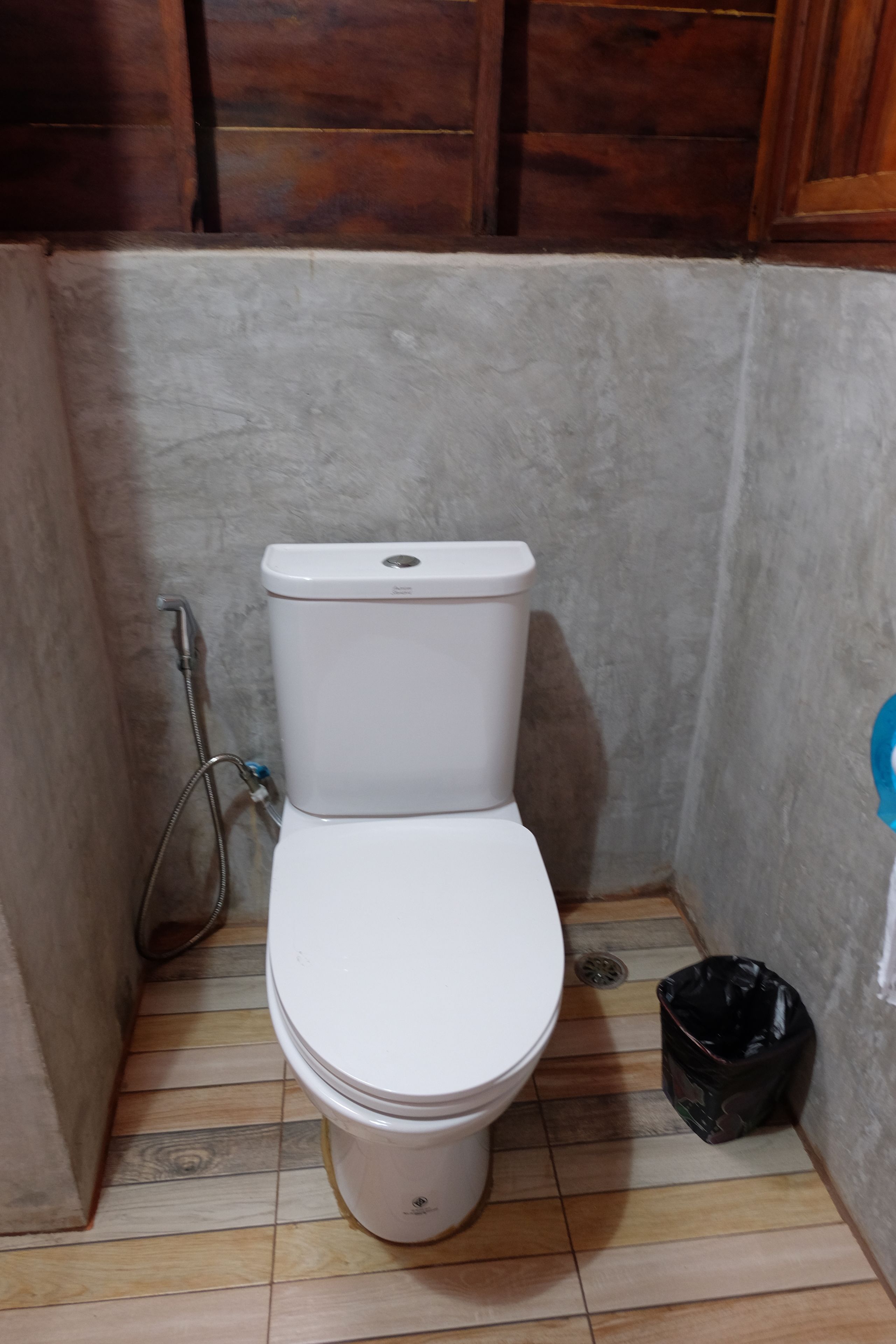 A small, enclosed bathroom with a white toilet, a showerhead, and a black trash bin.