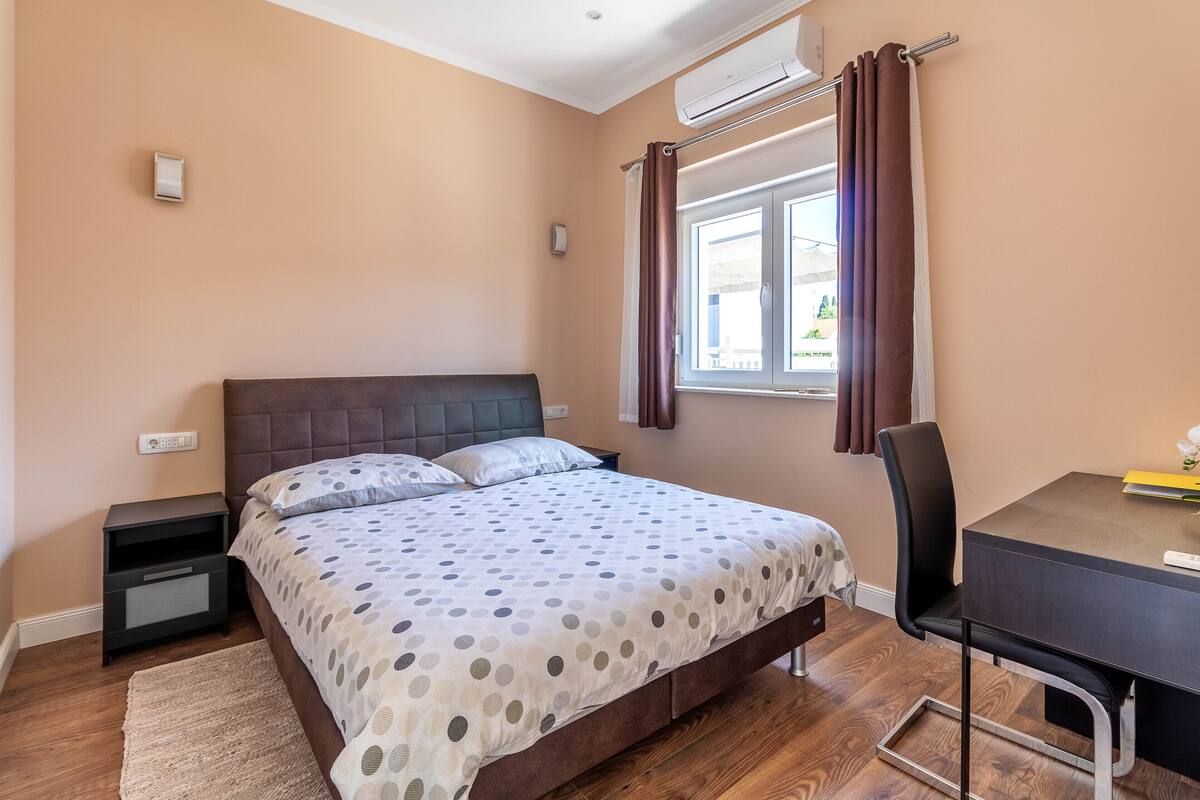 A bedroom with a bed, bedside table, chair, and a desk with a chair.