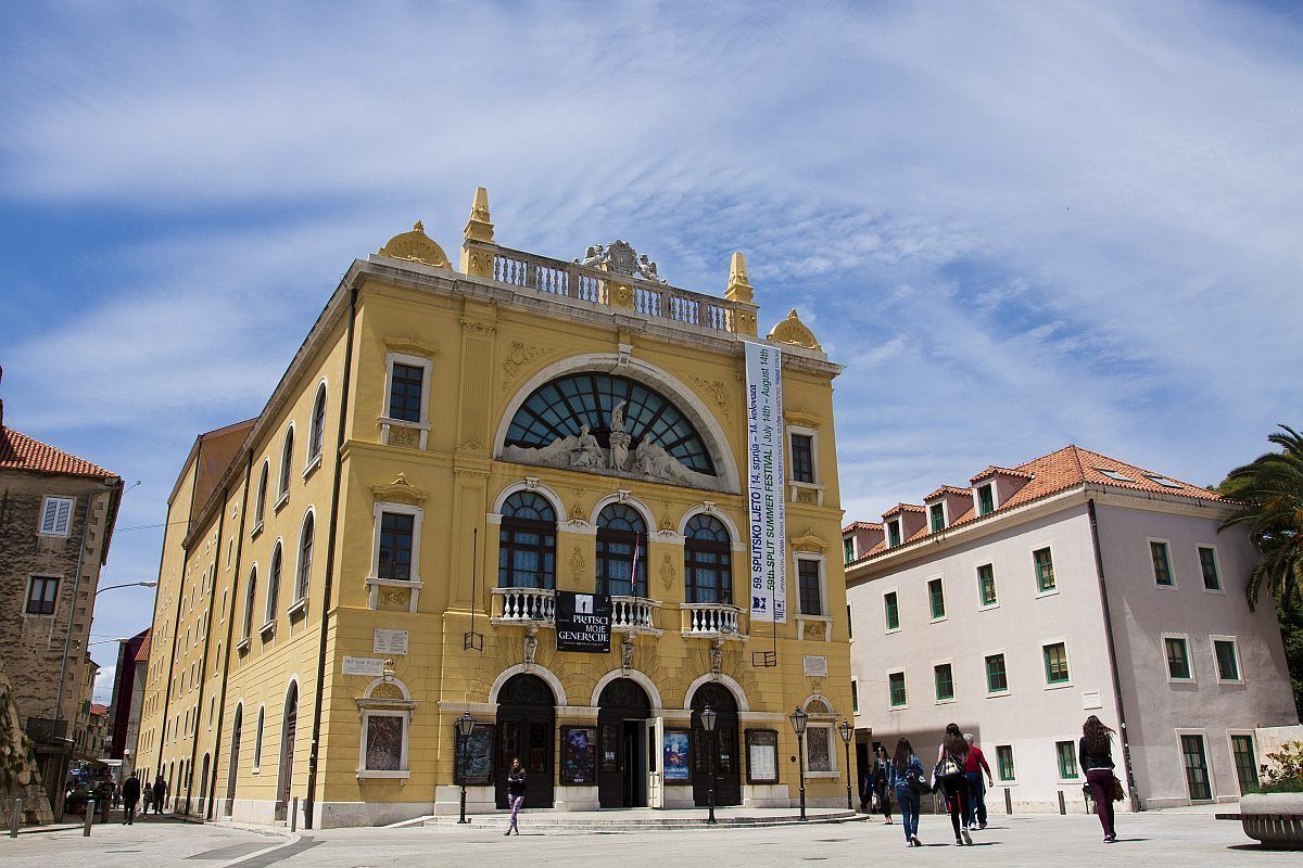 A historic building with a central archway, multiple balconies, and a sign indicating a cultural event.