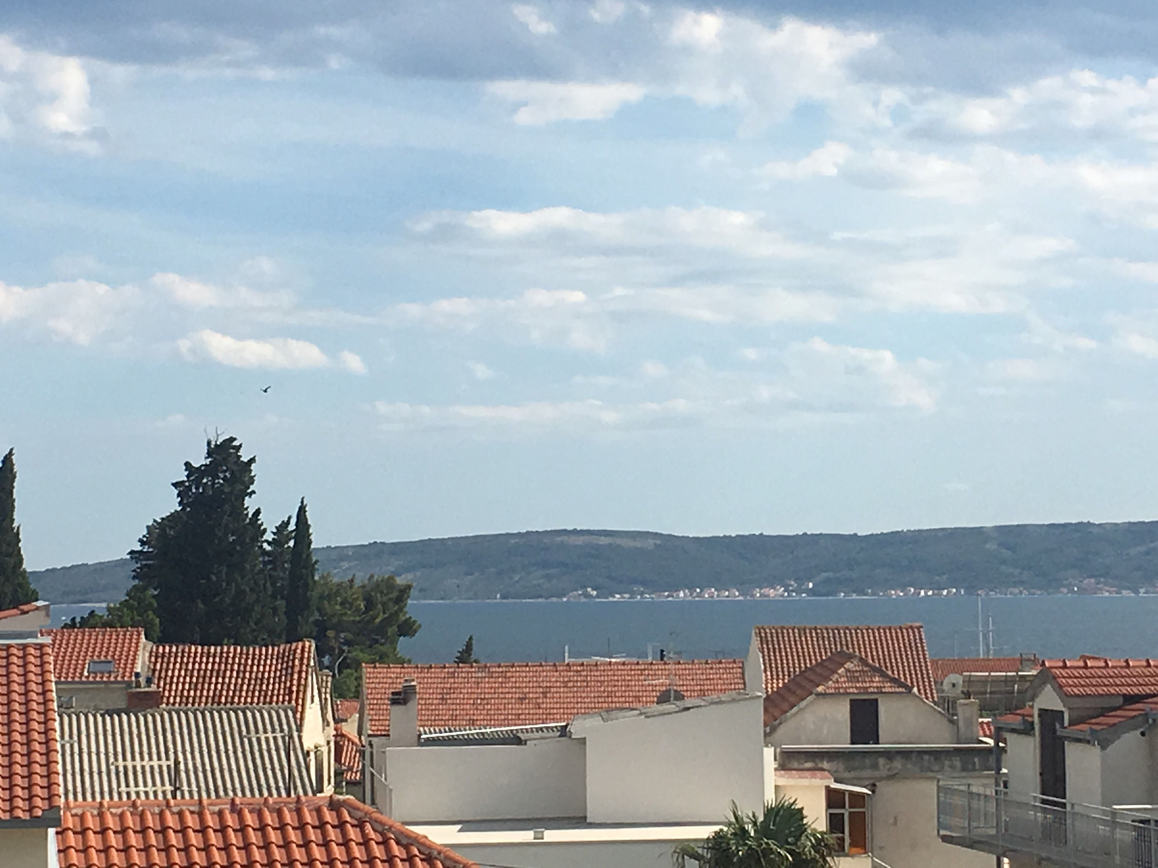 A coastal residential area with red-tiled roofs, a clear sky, and a view of the sea in the background.