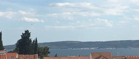 A coastal residential area with red-tiled roofs, a clear sky, and a view of the sea in the background.