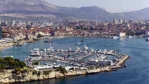 A marina with numerous boats docked, surrounded by a cityscape with buildings and mountains in the background. - Stay Split Bay (Kastela)