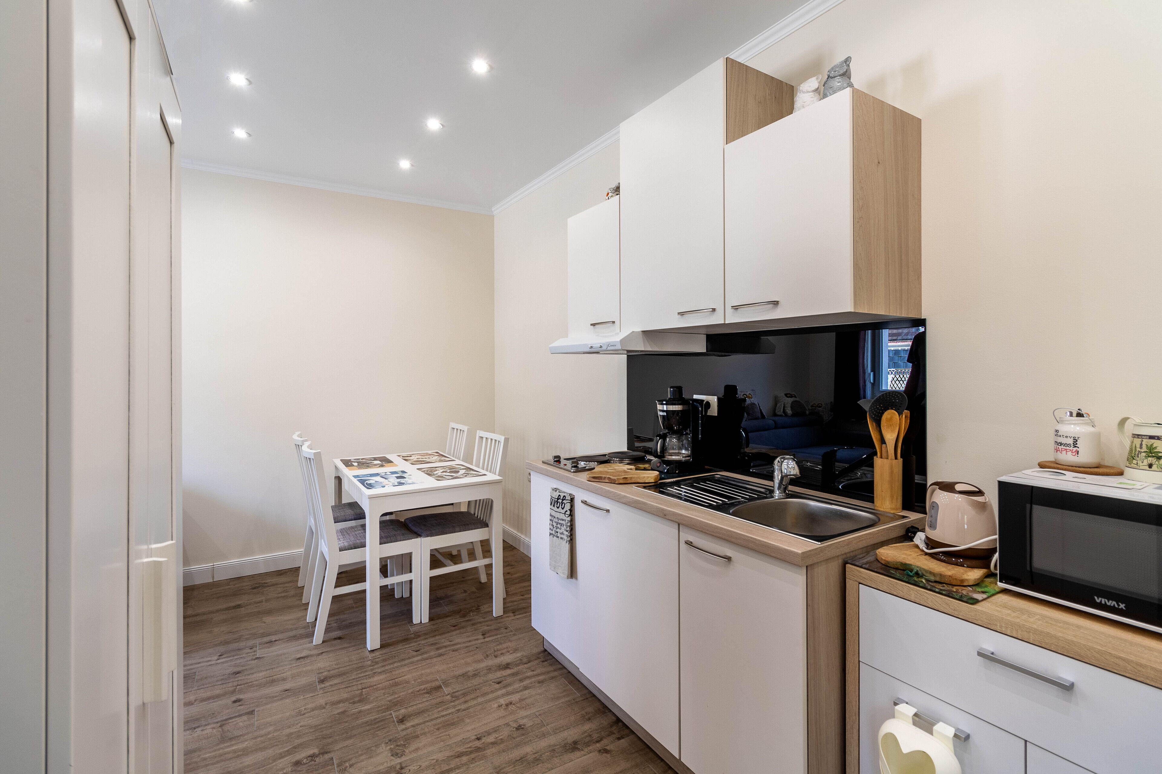 Una cucina compatta con mobili bianchi, un forno a microonde e un'area pranzo con tavolo e sedie.