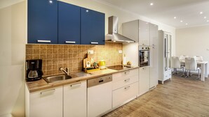 A modern kitchen with blue cabinets, a built-in oven, and a dining area with a white table and chairs. - Stay Split Bay (Kastela)