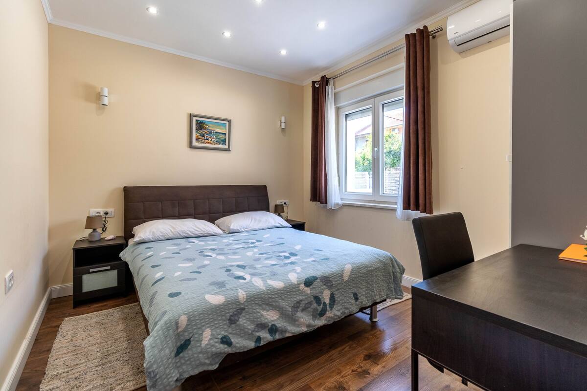 A bedroom with a bed, bedside table, lamp, and a desk with a chair.