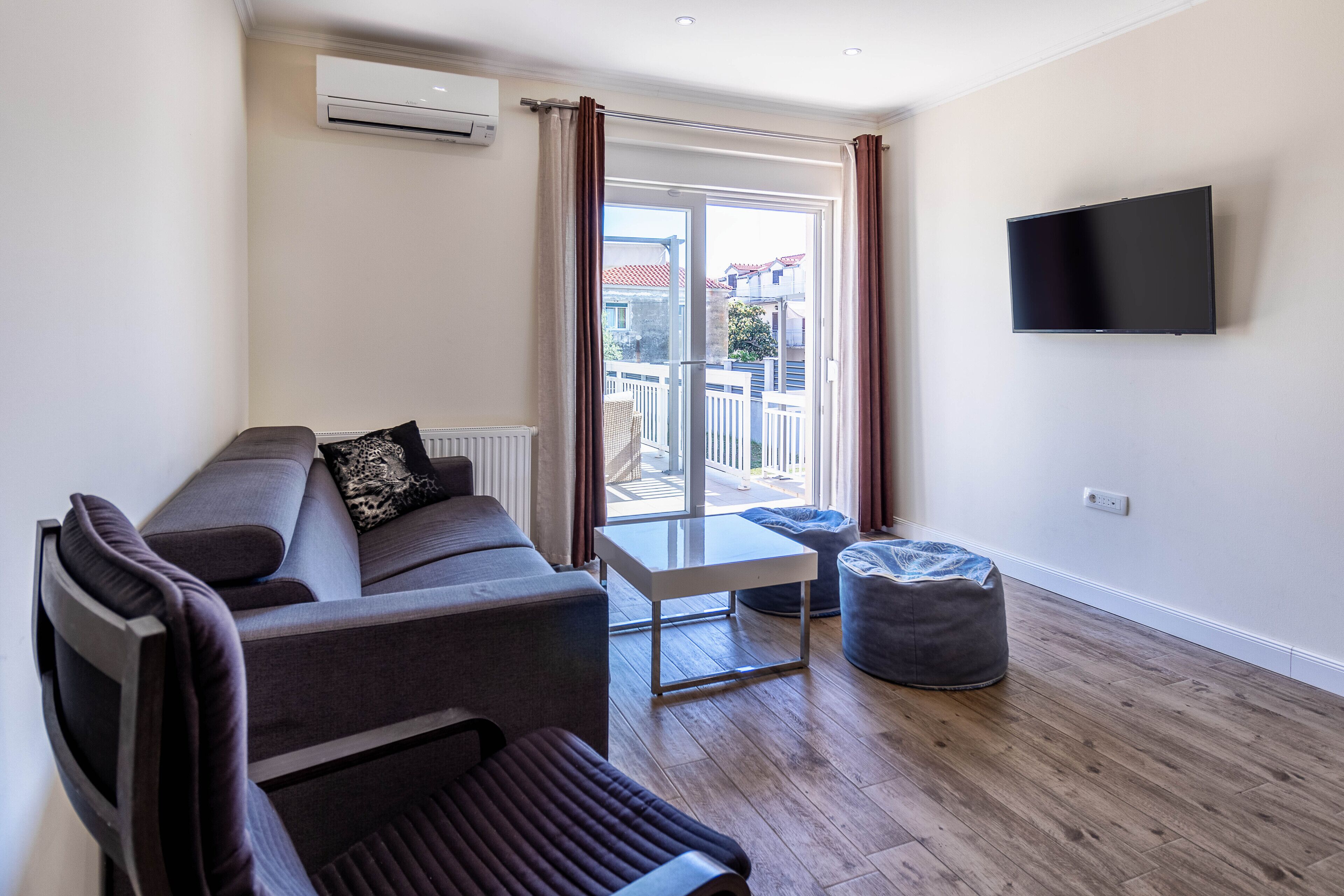 A modern living room with a sofa, a small table, a bean bag, and a TV mounted on the wall.