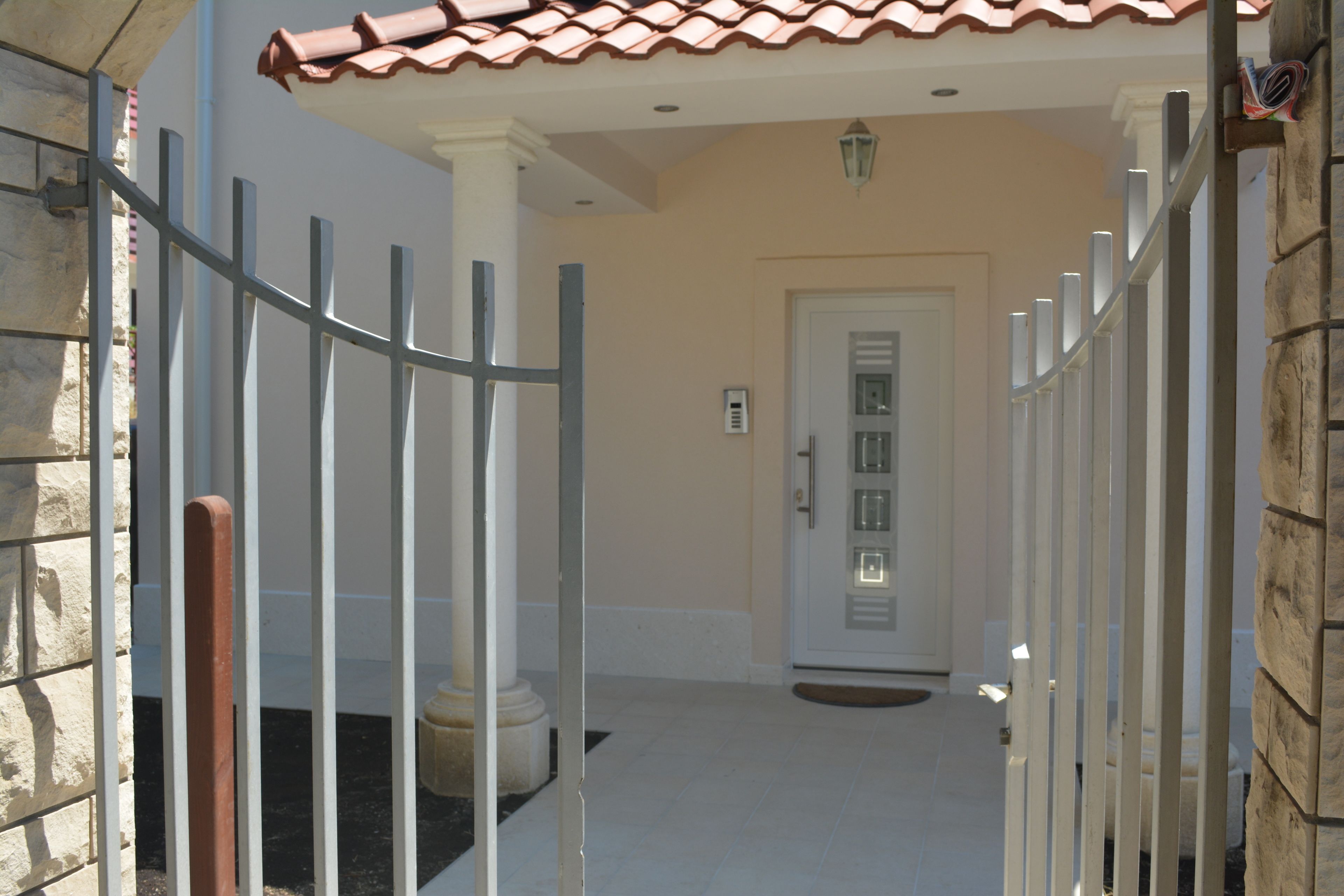 A gated entrance with a white door, a stone wall, and a tiled roof.