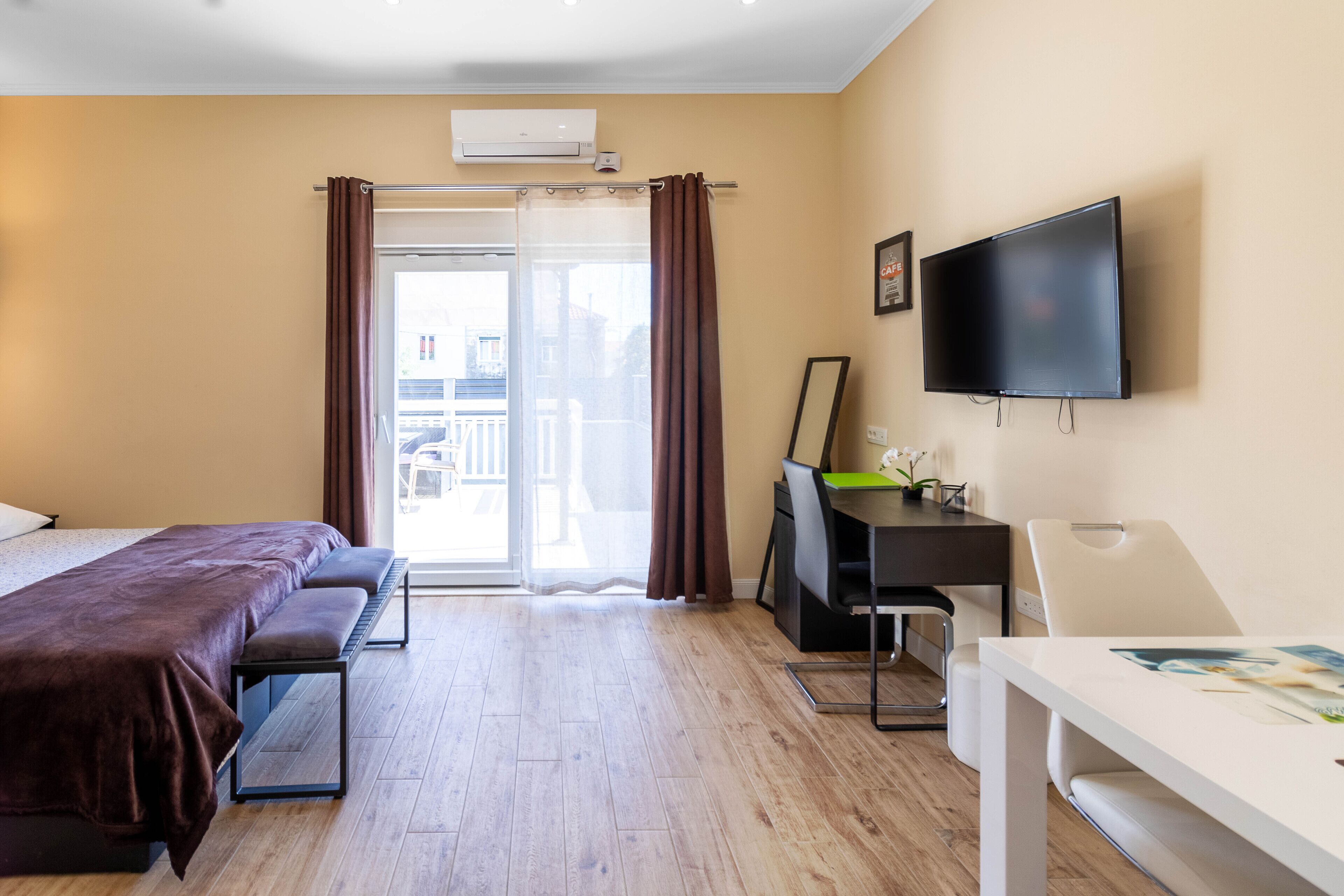 A hotel room with a bed, a desk, a chair, a TV, and a balcony with curtains.