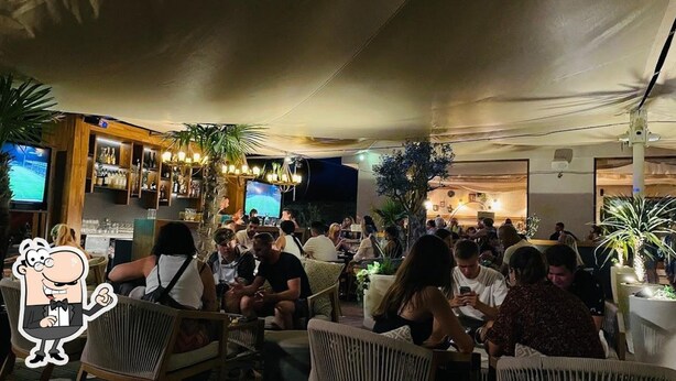 An outdoor dining area with wicker furniture, a bar with bottles, and a TV screen. - Stay Split Bay (Kastela)