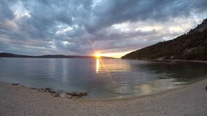 A calm lake with a sunset, a sandy beach, and a forested hillside. - Stay Split Bay (Kastela)