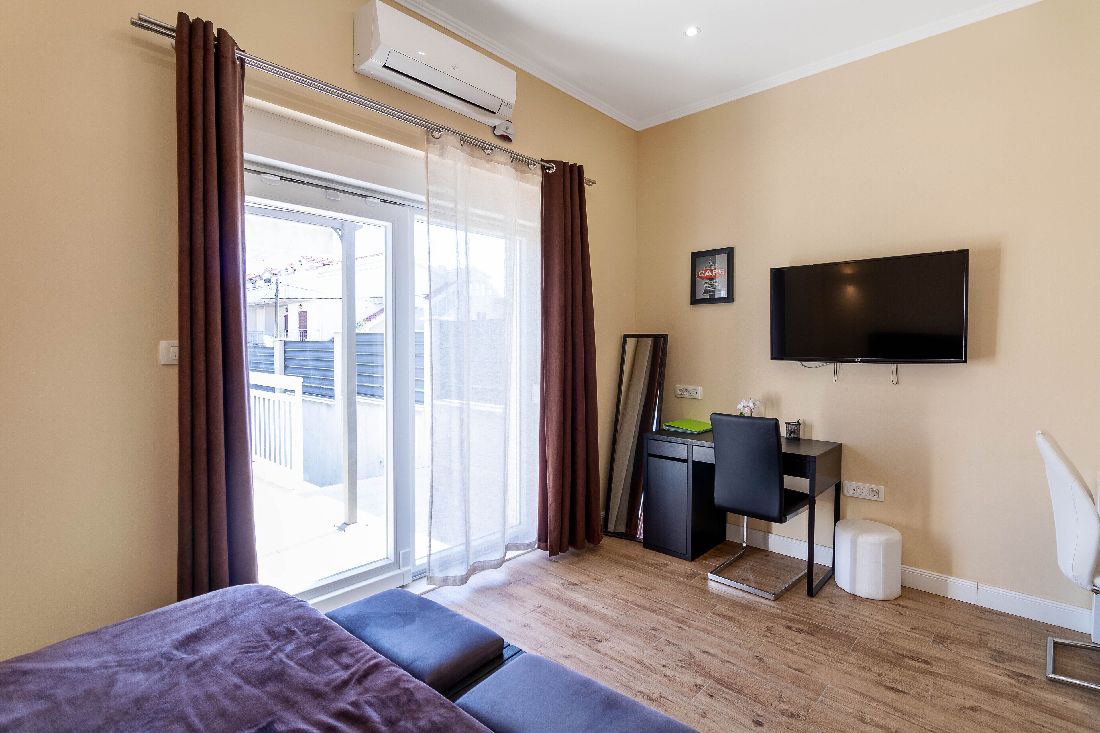 A modern hotel room with a bed, a desk, a chair, a TV, and a sliding glass door with curtains.