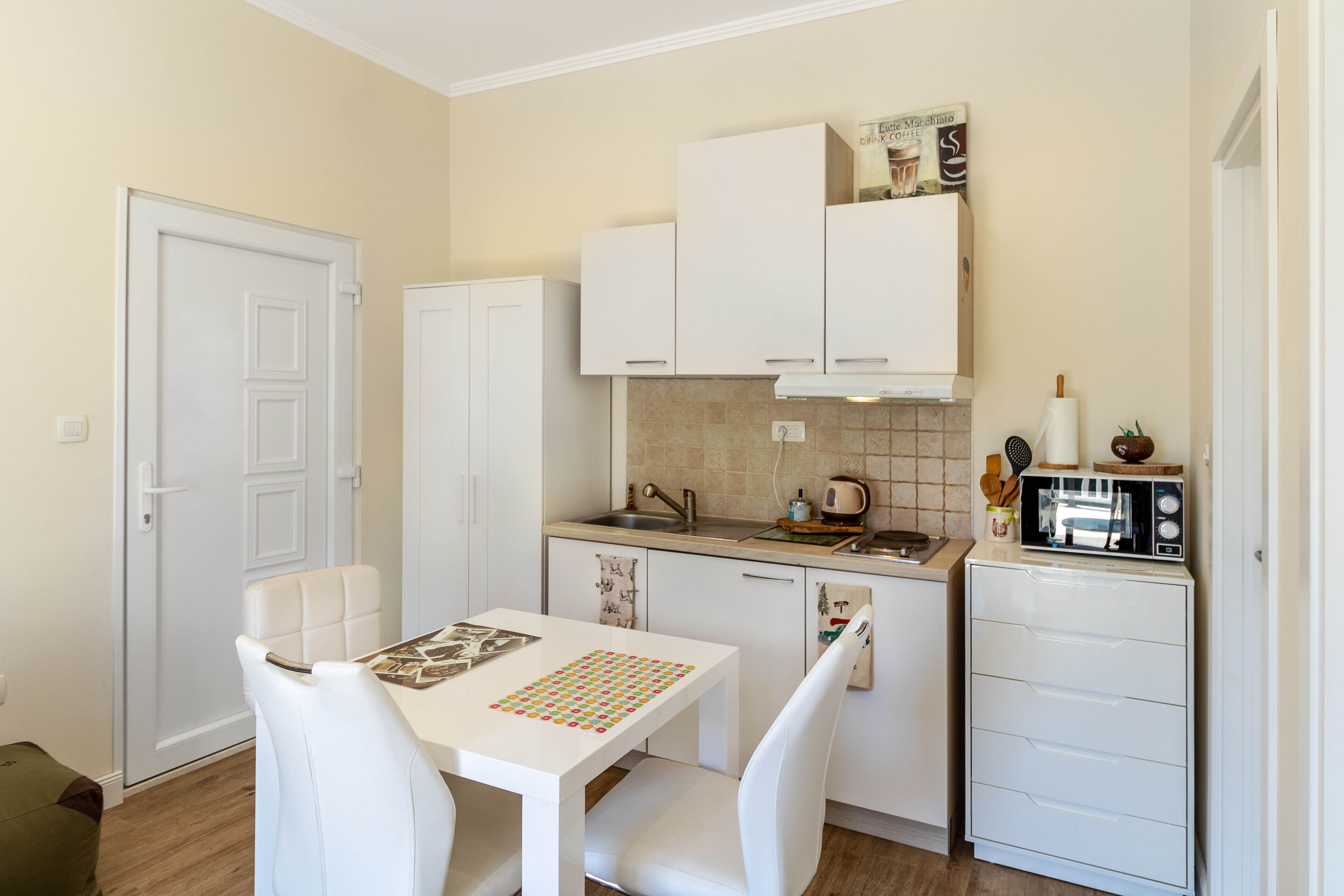 A compact kitchen with white cabinetry, a dining table with chairs, and a microwave on the countertop.