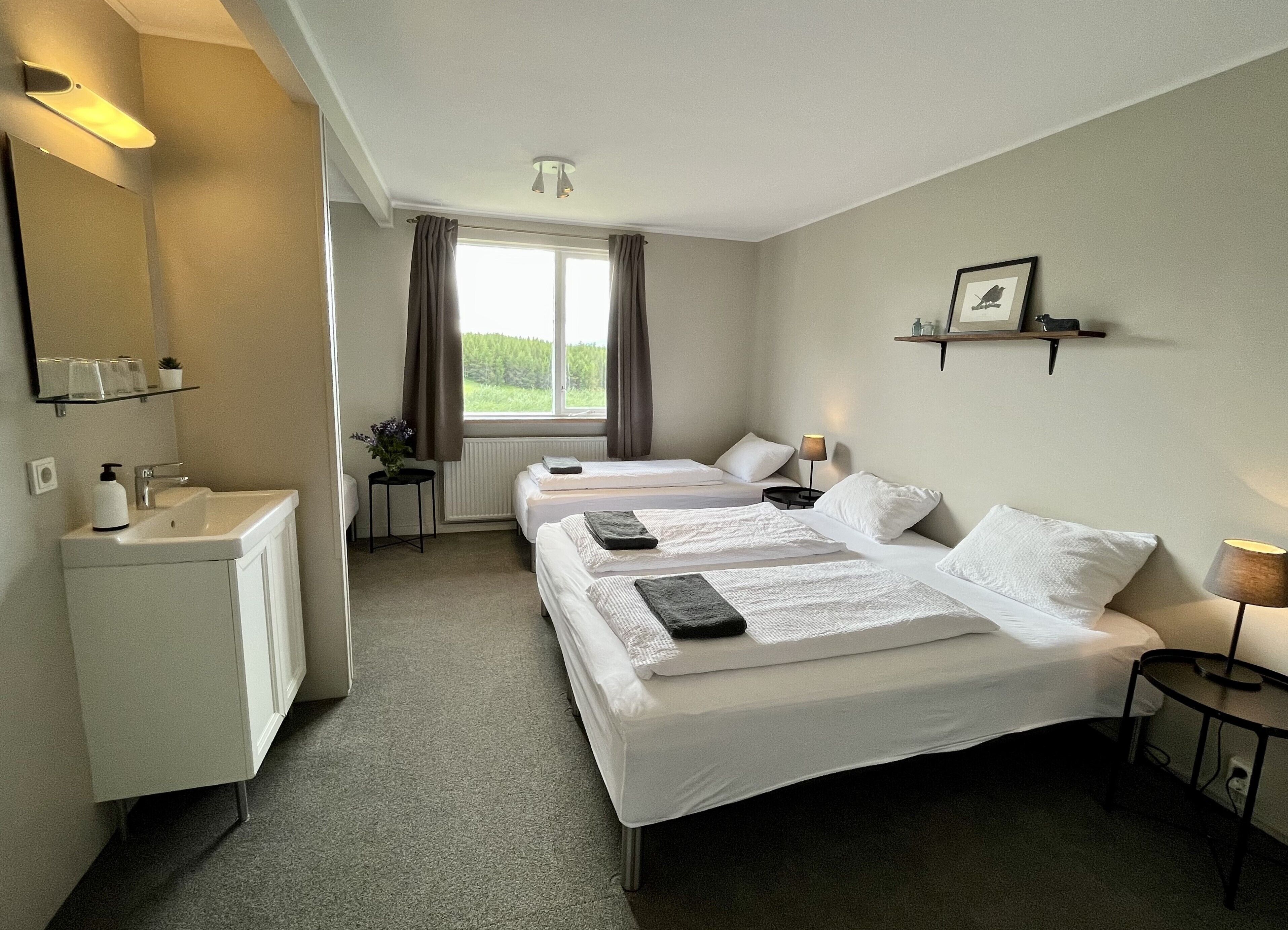 A hotel room with two beds, a small desk, a mirror, and a window with curtains.