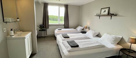 A hotel room with two beds, a small desk, a mirror, and a window with curtains.